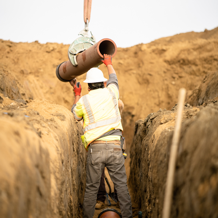 Turf Construction employee guiding vitrified clay pipe into sewer trench.