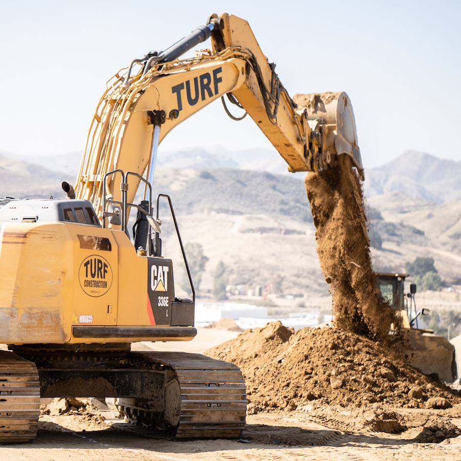 Turf Construction Caterpillar 336 excavator dumping dirt out of bucket on job site.