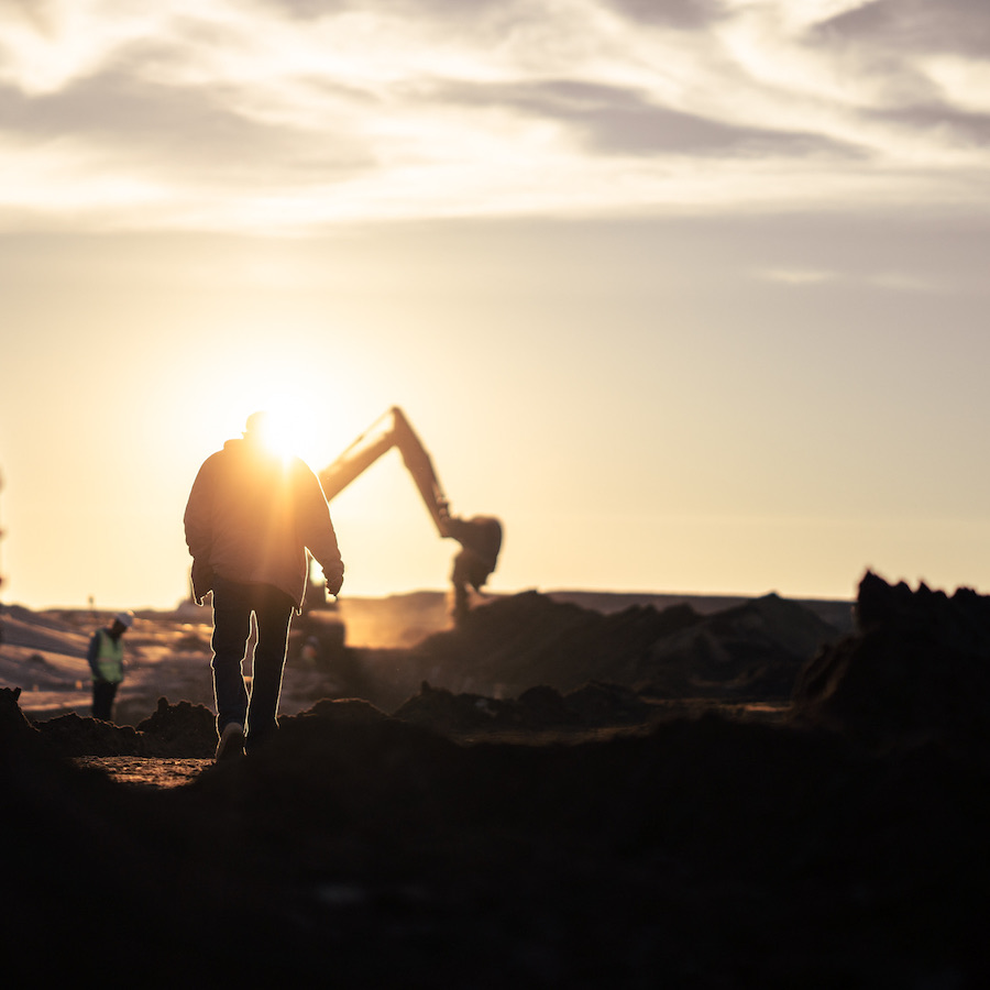 Artistic photograph of Turf Construction employee with excavator in the background during sunrise.