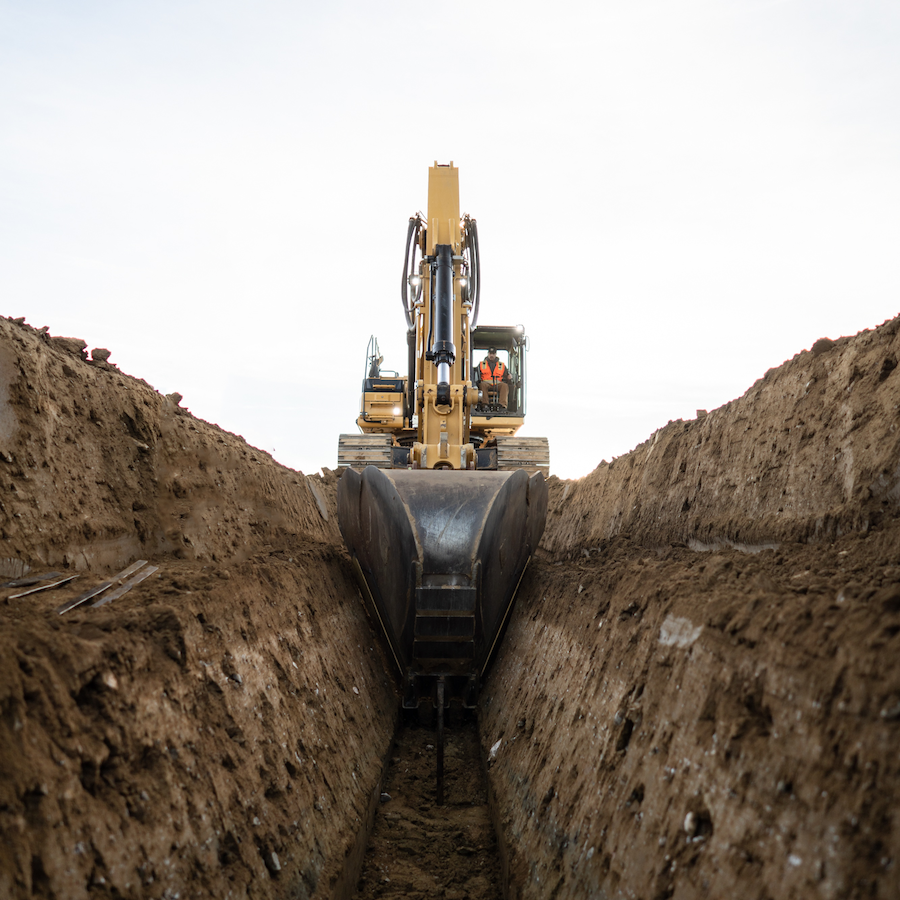 Turf Construction employee digging underground utility trench with Caterpillar 336 excavator.