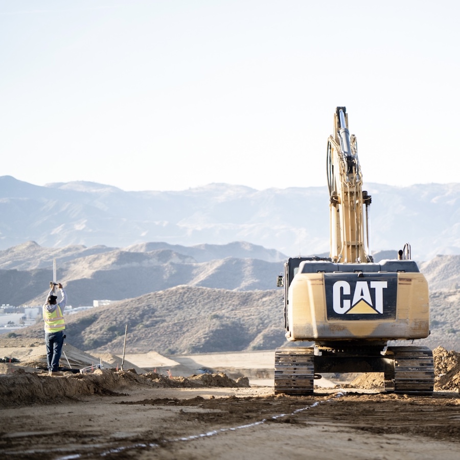Turf Construction employee standing next to Caterpillar 336 excavator on job site with scenic view.