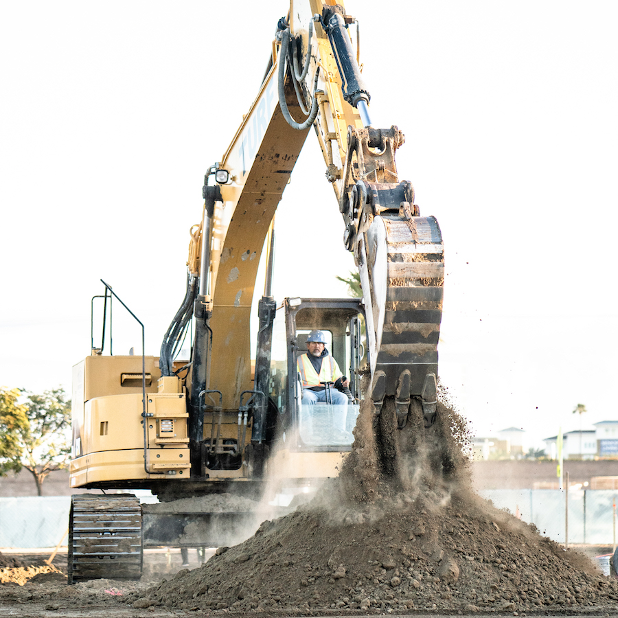 Turf Construction Caterpillar 328 excavator with operator dumping dirt out of bucket on job site.